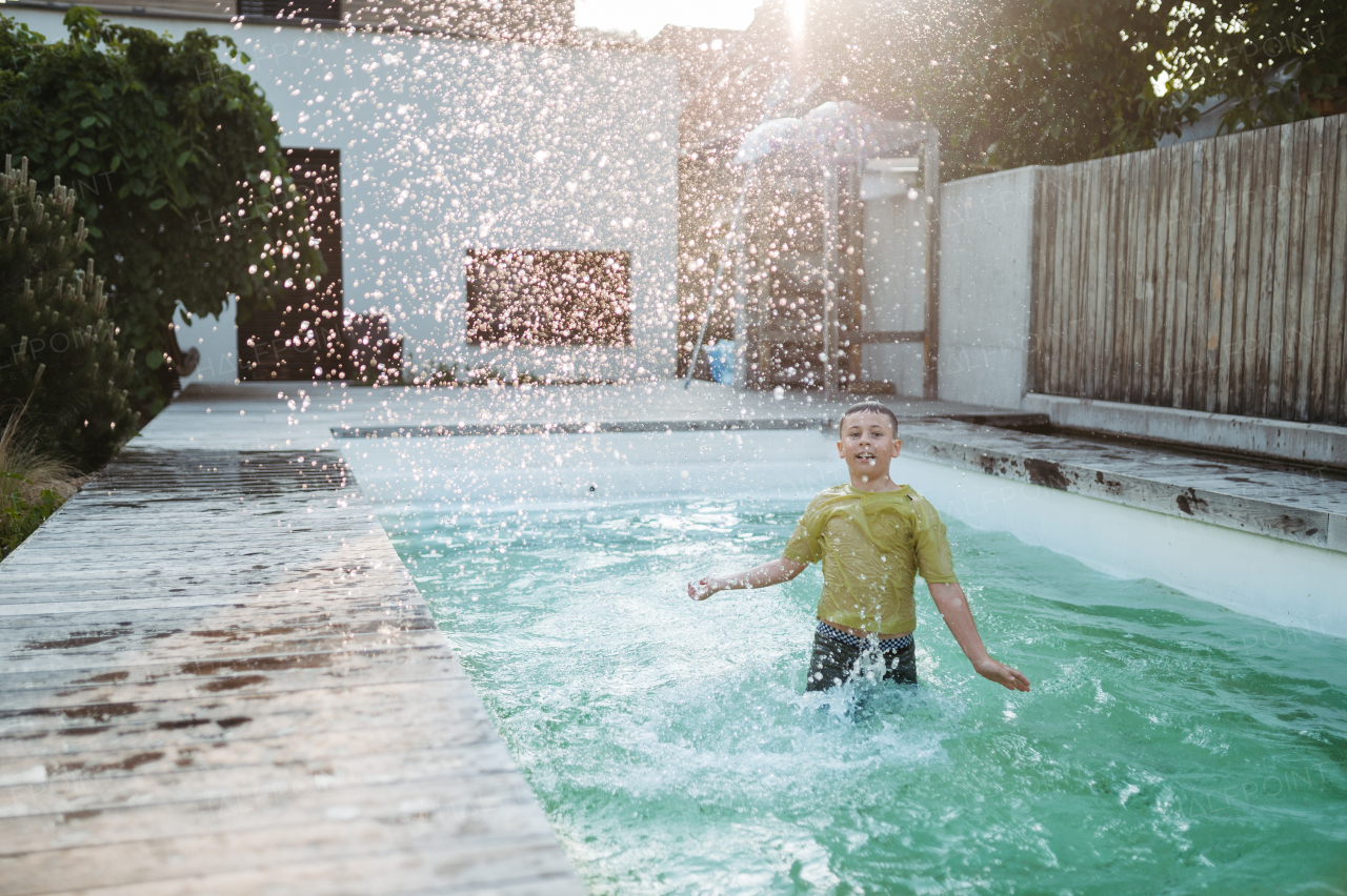 Young dressed boy jumping in the swimming pool and splashing water. Pool safety with childrens. Boy slipped on the wet floor and fell into the pool.