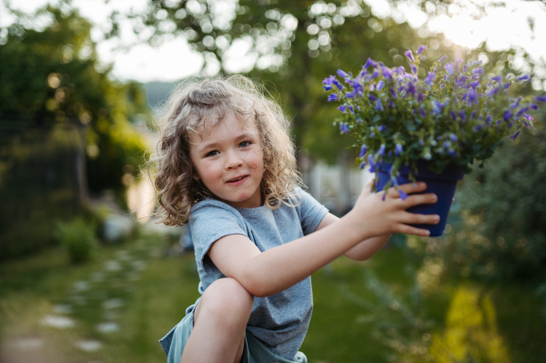 Potrait of little girl taking care of flowers in the garden, holding purple flower bells in pot.