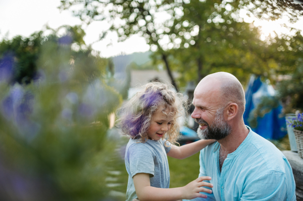 Father and daughter taking care of plants in the garden, enjoying summer flowers. Dad and daughter spending quality time together, bonding.