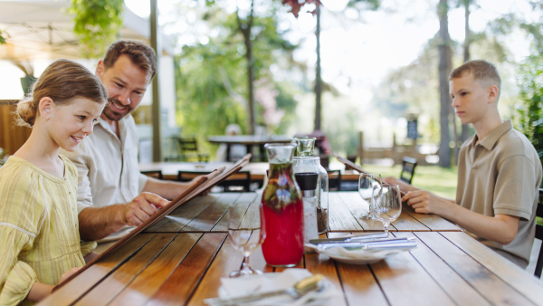 Father and kids reading menus in a restaurant, choosing food and drinks. Family dinner at a restaurant.