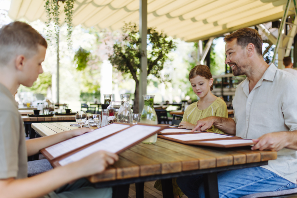 Father and children choosing food from menu. Single-parent family having dinner at a restaurant. Concept of Father's Day.