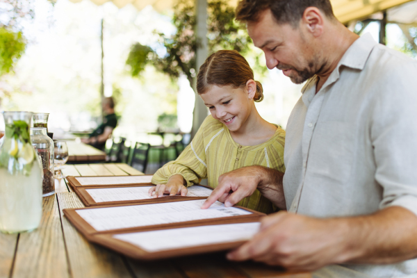 Father and daughter reading menus in a restaurant, choosing food and drinks. Family dinner at a restaurant.