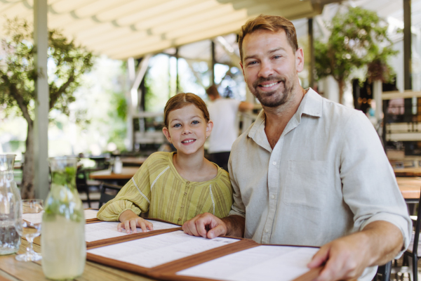 Father and daughter reading menus in a restaurant, choosing food and drinks. Family dinner at a restaurant.