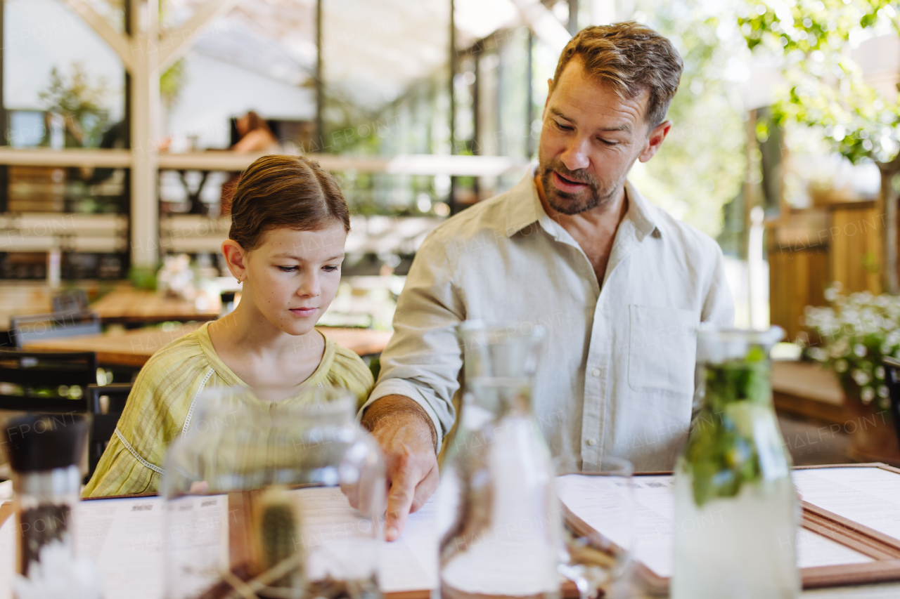 Father and daughter reading menus in a restaurant, choosing food and drinks. Family dinner at a restaurant.