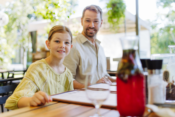 Father and daughter reading menus in a restaurant, choosing food and drinks. Family dinner at a restaurant.