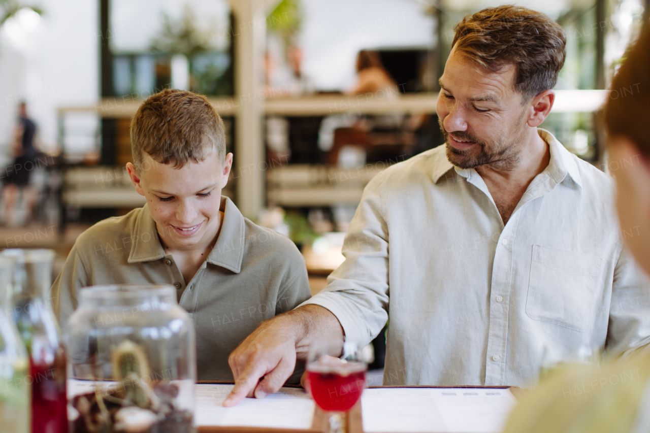 Father and son reading menus in a restaurant, choosing food and drinks. Family dinner at a restaurant.