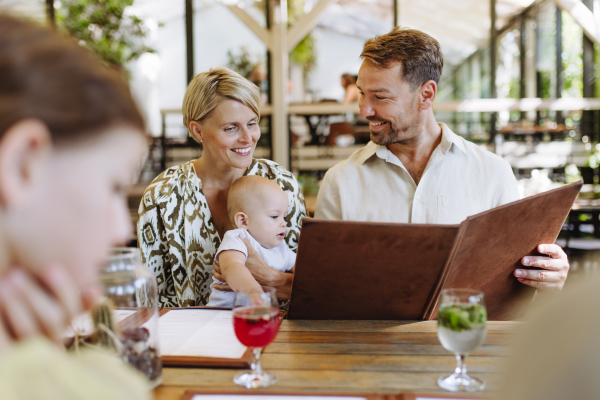 Family with baby and daughter reading menus in a restaurant, choosing food and drinks. Family dinner at a restaurant.