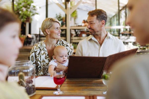 Family with baby and daughter reading menus in a restaurant, choosing food and drinks. Family dinner at a restaurant.