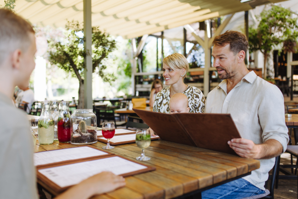 Family with baby and daughter reading menus in a restaurant, choosing food and drinks. Family dinner at a restaurant.