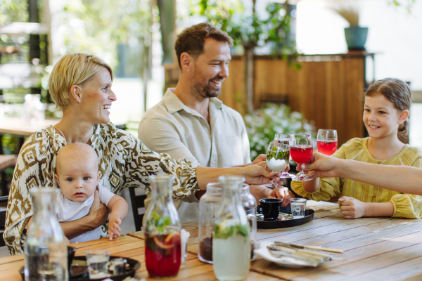 Family with children and a small baby clinking with galsses in a restaurant. A small family celebration in family friendly restaurant.