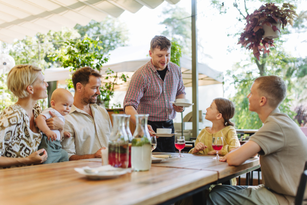 Waiter bringing food to the table in the restaurant. Family having dinner at a restaurant.