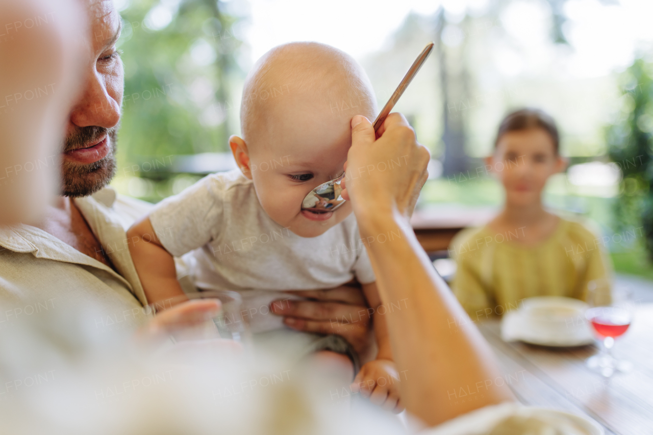 A small baby is being fed soup with a big spoon. The mother feeding the young child in a restaurant.