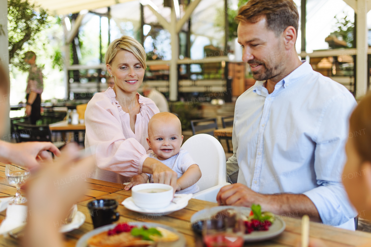 Family with baby in high chair eating food at restaurant. Family dinner at a restaurant.