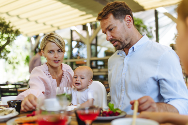 Family with hungry baby in high chair eating food at restaurant. Family dinner at a restaurant.