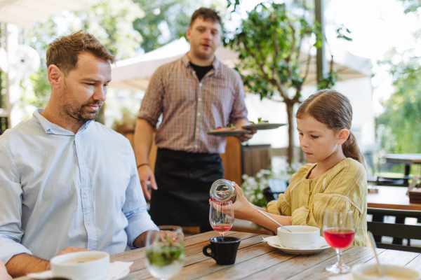 A girl pouring a drink from a bottle into a glass for her father. A family lunch in a family-friendly restaurant.