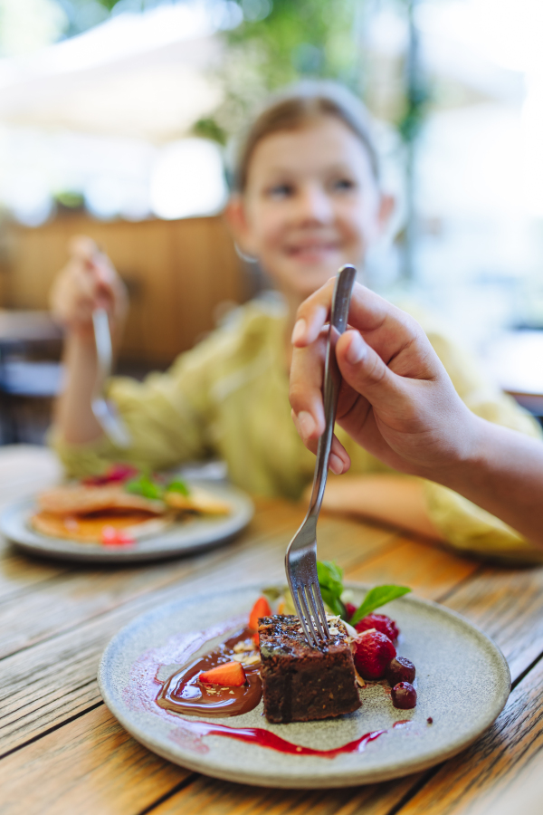 Close-up shot of a plate with chocolate brownie cake. Girl eating pancakes in a restaurant. Family dinner in a family-friendly restaurant.