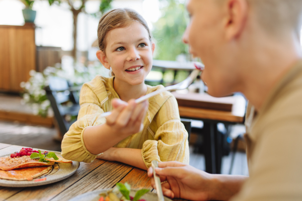 Sister offering a piece of dessert to her brother for a taste. Family having dinner at a restaurant.