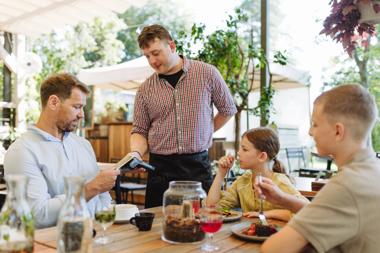 Man paying for lunch in a restaurant, paying by card. Holding card near terminal card reader.