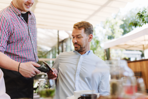 Man paying for lunch in a restaurant, paying by card. Holding card near terminal card reader.