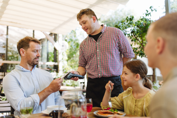 Man paying for lunch in a restaurant, paying by card. Holding card near terminal card reader.