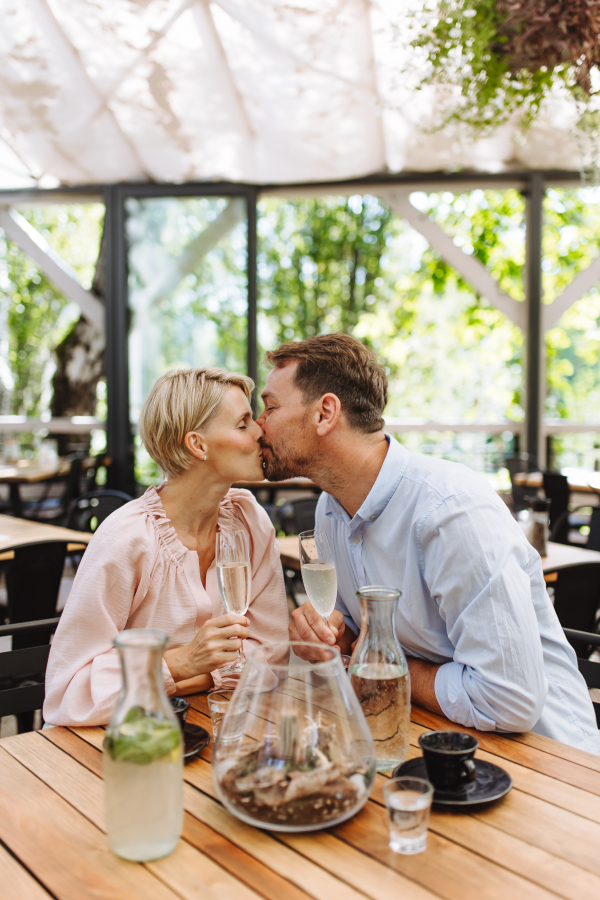 Close up of beautiful couple in a restaurant, on a romantic date. Wife and husband kissing, having a romantic moment at restaurant patio.