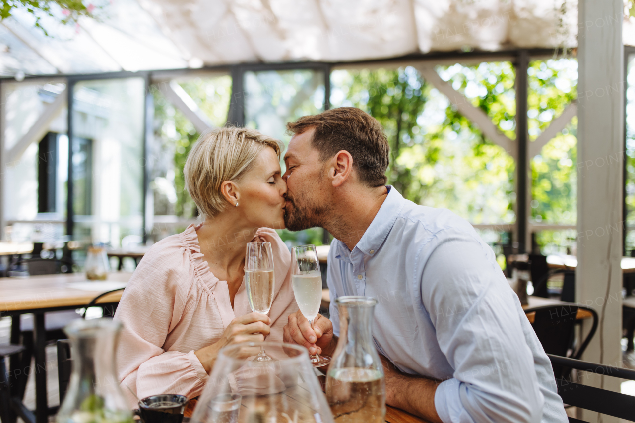 Close up of beautiful couple in a restaurant, on a romantic date. Wife and husband kissing, having a romantic moment at restaurant patio.