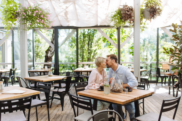 Beautiful couple in a restaurant, on a romantic date. Wife and husband kissing, having a romantic moment at restaurant patio.