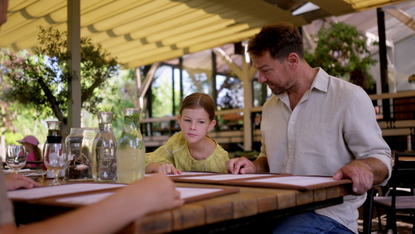 Father and daughter reading menus in a restaurant, choosing food and drinks. Family dinner at a restaurant.