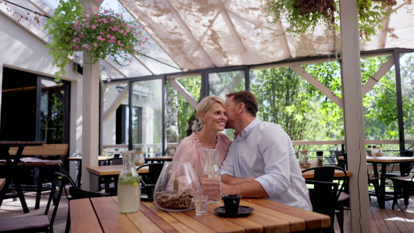 Video of beautiful couple in a restaurant, on a romantic date. Husband whispers into his wife's ear, having a romantic moment at restaurant patio.