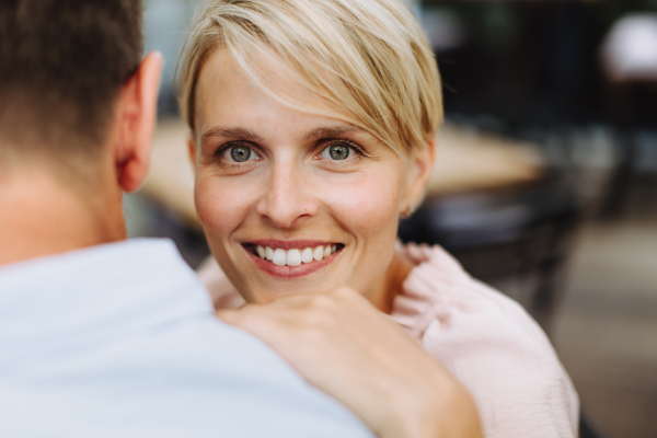 Portrait of beautiful couple in a restaurant, on a romantic date. Wife and husband touching foreheads, having a romantic moment at restaurant patio.