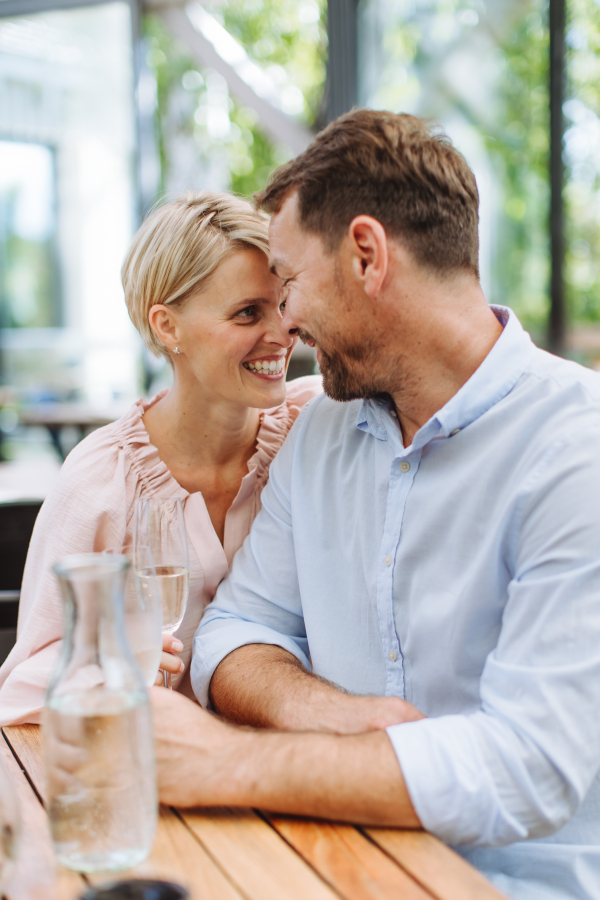 Portrait of beautiful couple in a restaurant, on a romantic date. Wife and husband touching foreheads, having a romantic moment at restaurant patio.