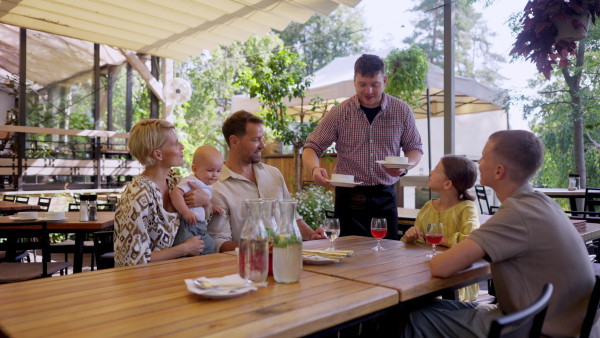 Waiter bringing food to the table in the restaurant. Family having dinner at a restaurant.