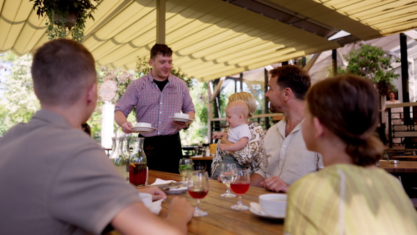 Waiter bringing food to the table in the restaurant. Family having dinner at a restaurant.