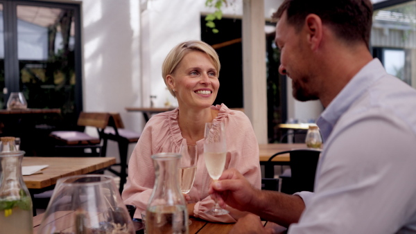 Video of beautiful couple in a restaurant, on a romantic date. Husband and wife are clinking champagne glasses, making a toast at restaurant patio.