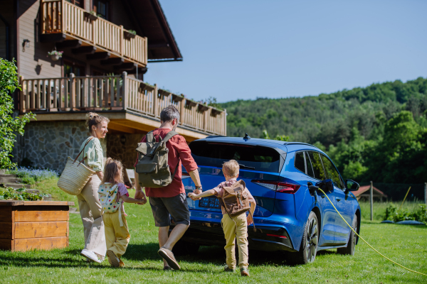 Happy family preparing for trip, charging their electric car.