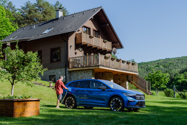 Man charging his electric car in the garden near his house.