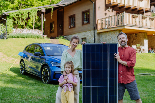 Happy family posing with a photovoltaics panel during their electric car charging.