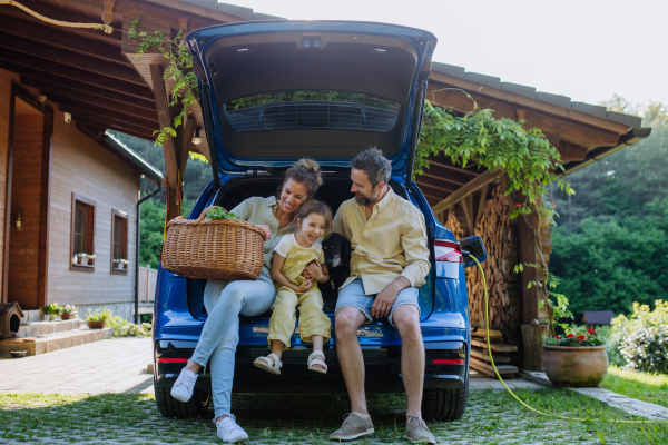 Happy family sitting in a car trunk and waiting for charging, preparationsfor picnic.