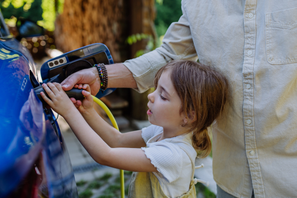 Father and his little daughter charging their electric car.