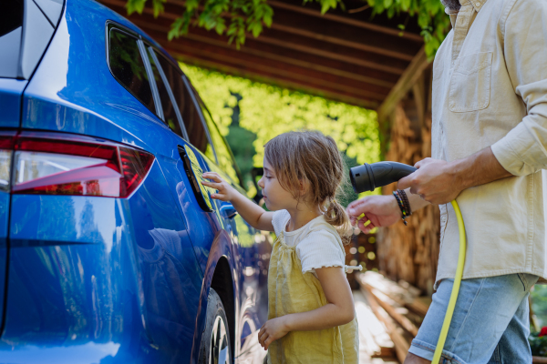 Father and his little daughter charging their electric car.