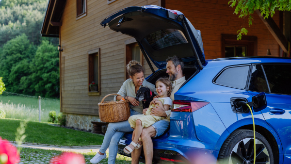 Happy family sitting in a car trunk and waiting for charging, preparationsfor picnic.