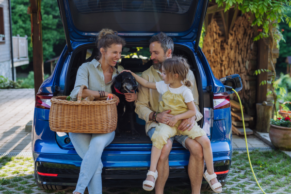 Happy family sitting in a car trunk and waiting for charging, preparations for picnic.