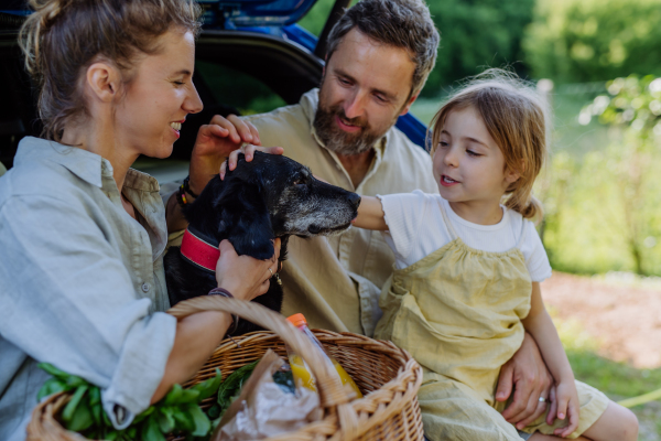 Happy family sitting in a car trunk stroking their dog.