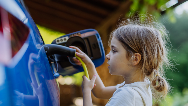 Little girl holding power supply cable and charging the electric car.