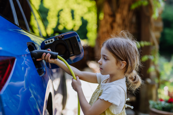 Little girl holding power supply cable and charging the electric car.