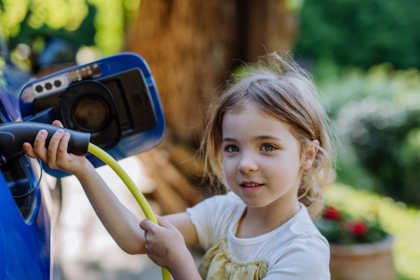 Little girl holding power supply cable and charging the electric car.