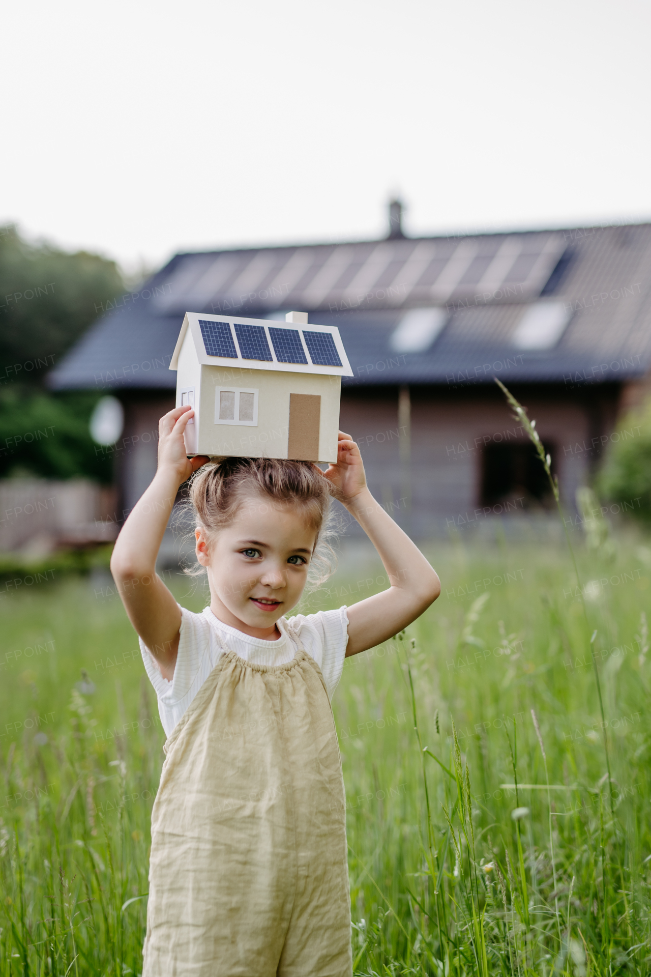 Portraitof little girl holding a model of house with solar panels, concept of sustainable lifestyle and renewable resources.