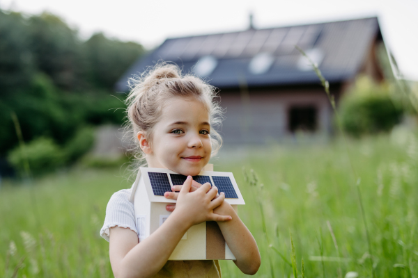 Portraitof little girl holding a model of house with solar panels, concept of sustainable lifestyle and renewable resources.