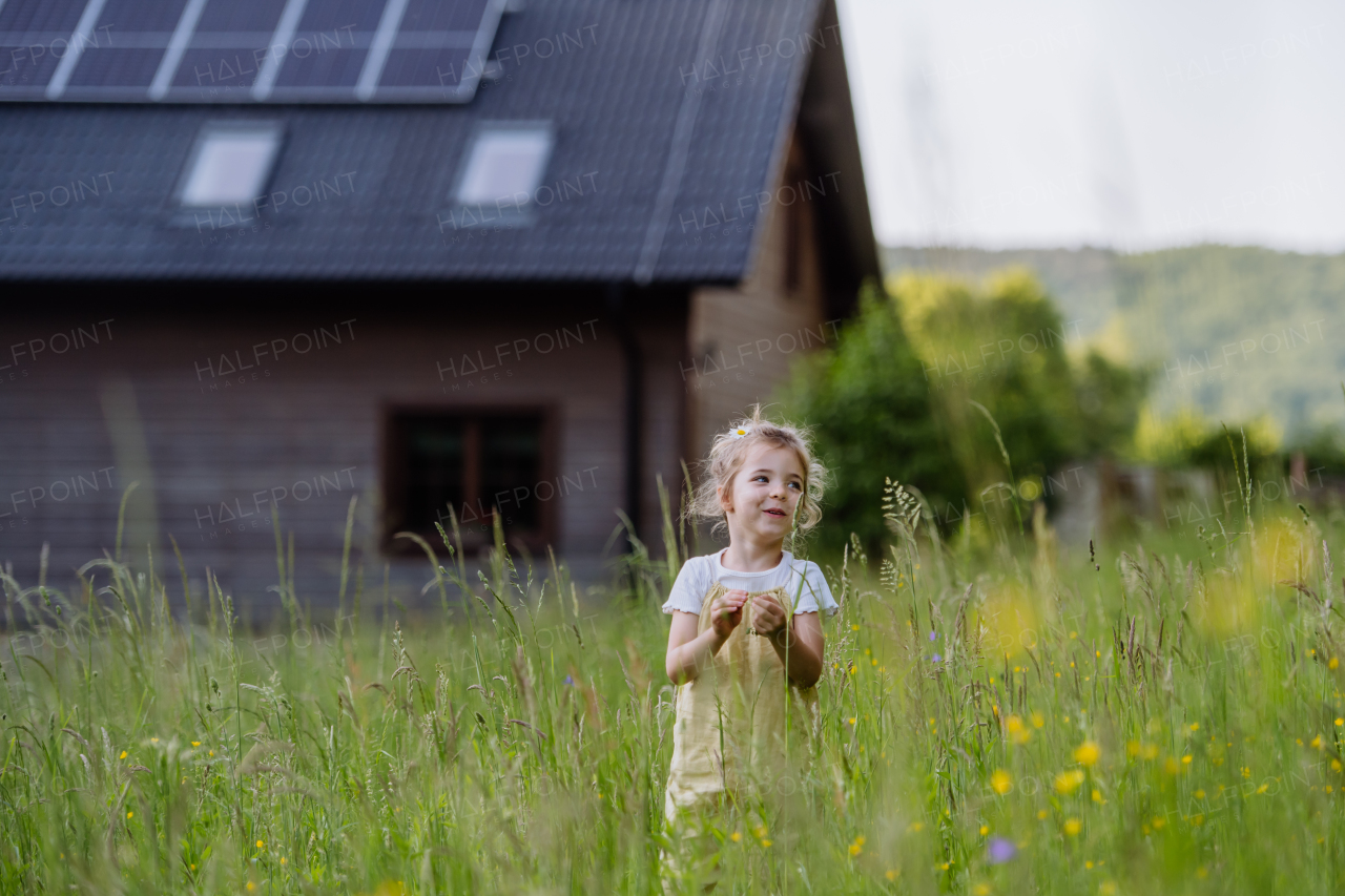 Portrait of a little girl in front of family house with solar panels, concept of sustainable lifestyle and renewable resources.