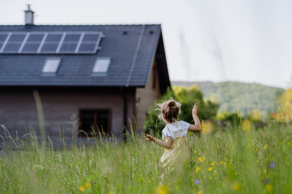 Rear view of a little girl in front of family house with solar panels, concept of sustainable lifestyle and renewable resources.